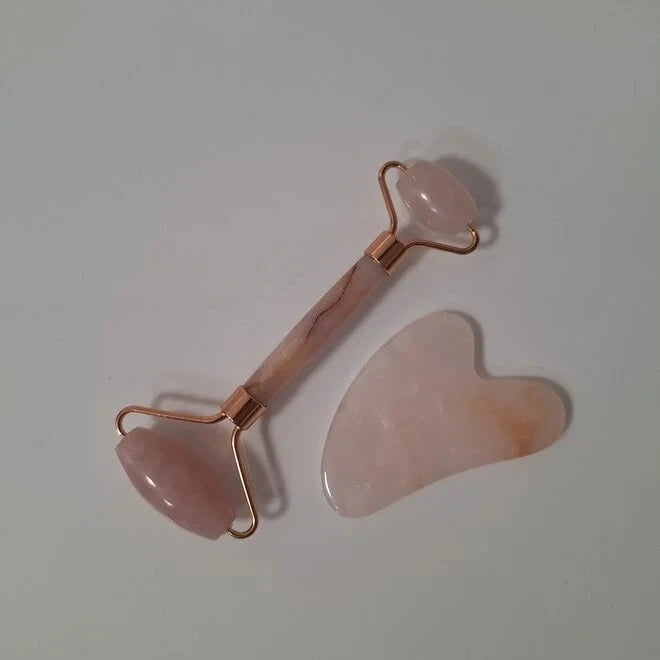 Rodillo facial y piedra gua sha de cuarzo rosa sobre fondo gris